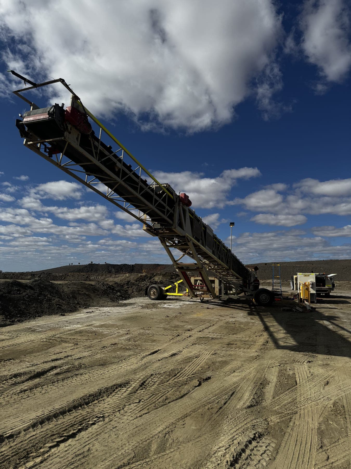 A mine-site conveyor and fixed plant against a wide blue sky.